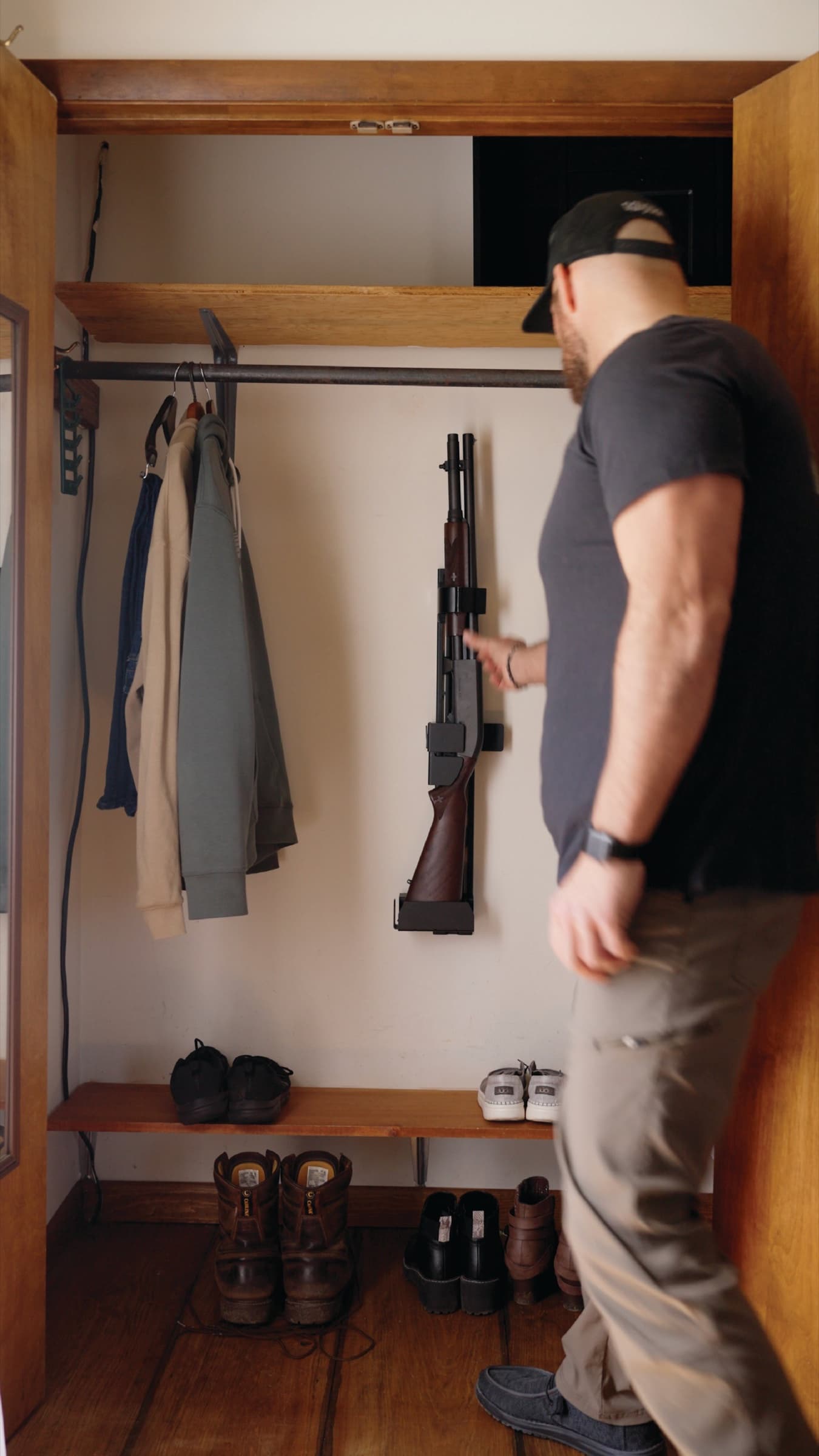 A man lifting a shotgun off a RACT mounted on the back wall of a coat closet