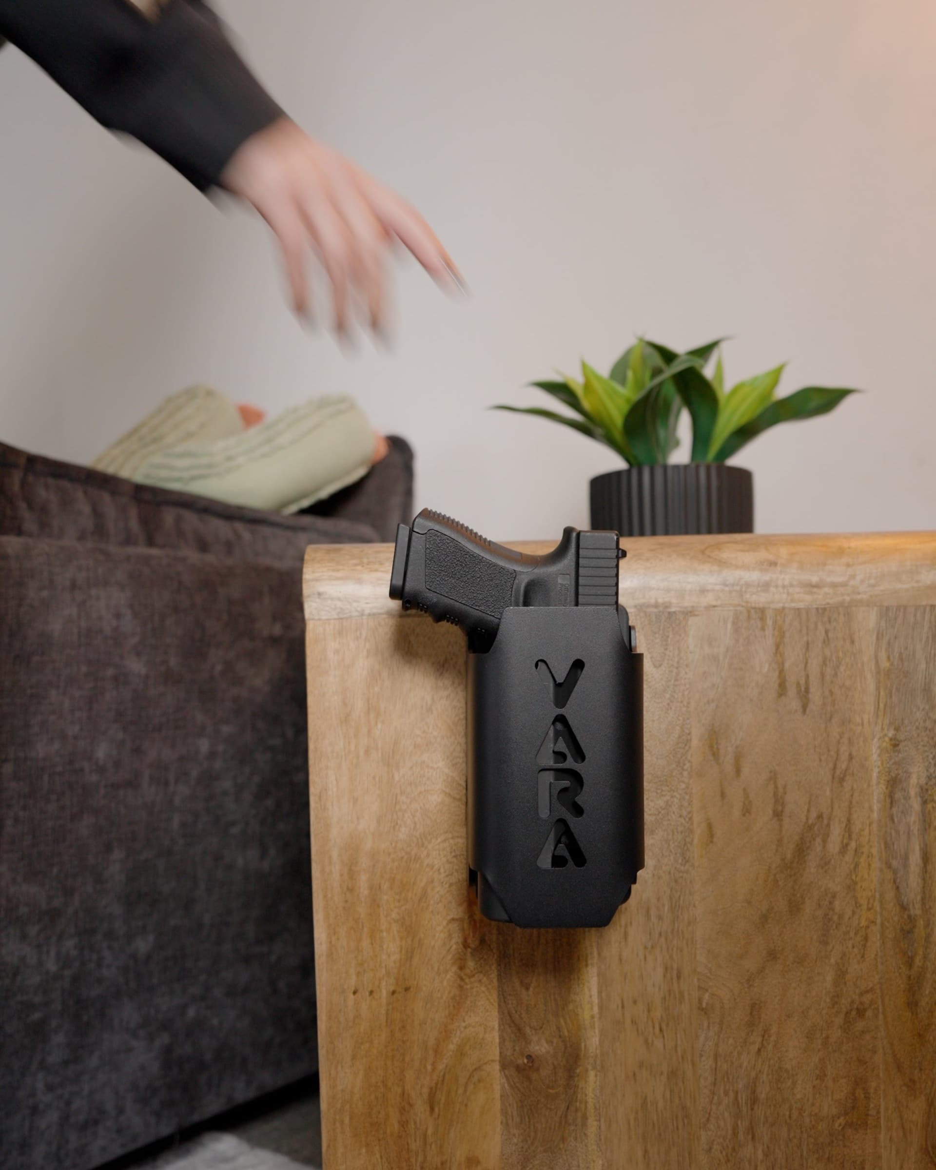 Reach Tactical mounted on the side of a wooden nightstand holding a pistol, a hand reaching down for it