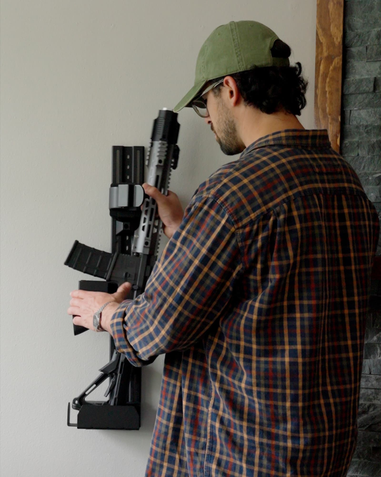 A man fitting the trigger cover over an AR-style rifle held in a RACT on his living room wall